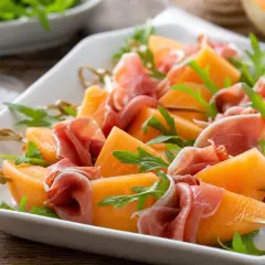 Melonenstücke mit Prosciutto und Rucola auf Spießen, perfekt als Snacks zum Wein.
