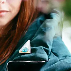 Kobieta w butelkowej zieleni z broszką w kształcie trójkąta z sukulentem.