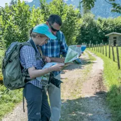 Zwei Wanderer mit Rucksäcken studieren eine Karte, um ihre Route zu planen. Die Packliste fürs Pilgern ist wichtig für die Tour.