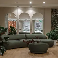 Nowoczesne oświetlenie w salonie fryzjerskim tworzy przytulną atmosferę. Wygodna, zielona sofa i bujna roślinność zapraszają do relaksu.