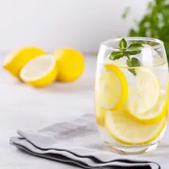 Orzeźwiająca woda z cytryną i miętą w szklance, obok leżą cytryny. Idealna na upalne dni.