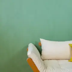 Ein Sofa mit weißen und gelben Kissen vor einer mintgrünen Wand. Die Frage "wieviel Wandfarbe pro qm" wird hier nicht beantwortet.