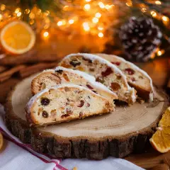 Tranches de stollen cake, un délice de Noël aux fruits secs et noix, saupoudré de sucre glace, sur une planche de bois, entouré de décorations festives.