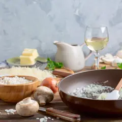 Préparation d'un risotto aux champignons, avec riz, oignons, champignons, parmesan, beurre et un verre de vin blanc.