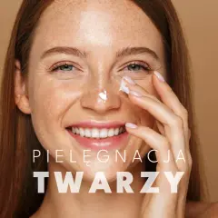 Uśmiechnięta kobieta z piegami nakłada krem na nos. To kluczowy element jej codziennego mycia twarzy i pielęgnacji.