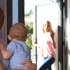 Mama z dzieckiem wita nianię, która przychodzi zapytać, ile kosztuje godzina opieki nad dzieckiem.