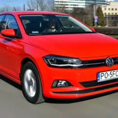 Czerwony Volkswagen Polo 6 w ruchu miejskim. Kierowca w szarej bluzie prowadzi auto.