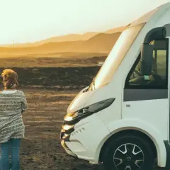Une femme seule face à un camping-car dans un paysage désertique au coucher du soleil. Un lieu à éviter en camping-car pour son isolement.
