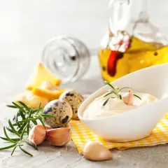 Kremowy sos aioli z czosnkiem i rozmarynem, obok jaj przepiórczych i butelki oliwy.