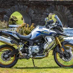 Moto Voge 500DS, una moto china con motor BMW, lista para la aventura junto a un puente de piedra y un río.
