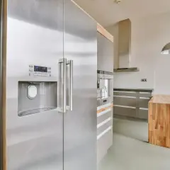 Nowoczesna kuchnia z lodówką w kolorze inox, drewnianą wyspą i stalowymi szafkami.