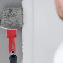 En målare använder en roller för att måla fasaden grå.