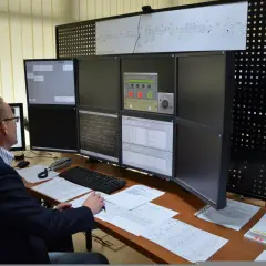Dyżurny ruchu PKP analizuje dane na wielu monitorach. Na biurku dokumenty i klawiatura.