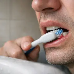 Primo piano di un uomo che si lava i denti subito dopo mangiato, con spazzolino e dentifricio.