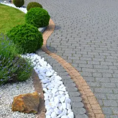 Piękny ogród z zadbanym trawnikiem, kwitnącą lawendą i ozdobnymi krzewami. Ścieżka z kostki brukowej, która wygląda jak po malowaniu, tworzy elegancką całość.
