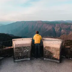 Un homme en jaune admire le panorama depuis le sommet du mont Aigoual, avec ses vastes étendues de montagnes bleues à perte de vue.