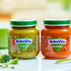 Dwa słoiczki BoboVita: brokuły i marchewka, idealne jako pierwsze pokarmy dla niemowląt po 4 miesiącu. Obok świeże warzywa.