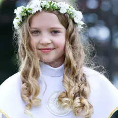 Dziewczynka w wianku z białych kwiatów, ubrana w białą komżę, gotowa do przyjęcia Komunii Świętej. W tle słychać piękne pieśni komunijne.