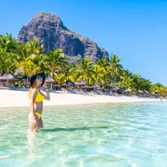 Frau im Bikini genießt das kristallklare Wasser an einem Traumstrand von Mauritius. Palmen und ein Berg im Hintergrund.