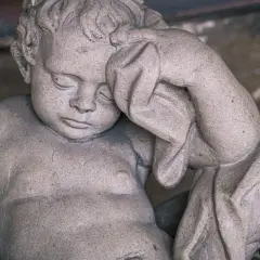 Kamienna rzeźba dziecka z zasłoniętymi oczami, jakby śniło o śmierci rodziców.