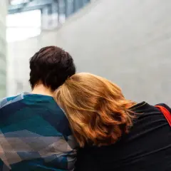 Osoba z rudymi włosami opiera głowę na ramieniu drugiej osoby. Widać tu pewną zależność w związku, potrzebę bliskości i wsparcia.