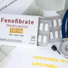 Opakowanie leku Fenofibrate 145 mg, tabletki, obok stetoskopu i wyników badań cholesterolu. Lipanthyl pomaga w leczeniu.
