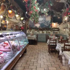 Wnętrze restauracji w stylu rustykalnym, z wiszącymi wędlinami i dekoracjami. W chłodni mnóstwo wyrobów, jak w najlepszym sklepie w Frascati.
