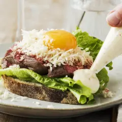 En lyxig smörgås med mört kött, äggula, sallad och riven ost. En klick krämig sås, kanske en carnitas cramby, spritsas på.