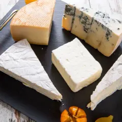 Assortimento di formaggi, tra cui un cremoso formaggio morbido, un erborinato e altri tipi, guarniti con frutta.