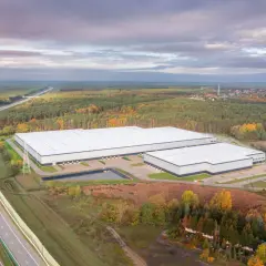 Nowoczesne, rozległe budynki firm magazynowych otoczone jesiennym lasem, w pobliżu autostrady.