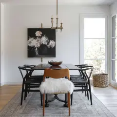Modern dining room ideas: a dark wood table with black wishbone chairs, a floral painting, and a fluffy white accent chair.