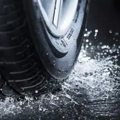 Koło samochodu na mokrej nawierzchni, rozpryskująca się woda. To zjawisko to aquaplaning, który może być niebezpieczny.
