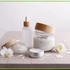 Kremy i serum w szklanych słoiczkach z bambusowymi nakrętkami, obok kwiatów. Składniki, jak ethylhexylglycerin, dbają o Twoją skórę.