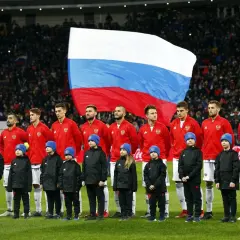 Piłkarze reprezentacji Rosji i dzieci w niebieskich czapkach stoją na murawie, za nimi ogromna flaga Rosji. Bah, piękny widok!