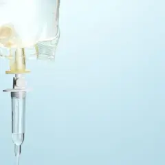 Kroplówka z płynem, symbolizująca żywienie pozajelitowe, zawieszona na jasnoniebieskim tle.