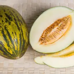 Un intero melone di Borgogna, tagliato a metà e a fette, mostra la sua polpa chiara e i semi dorati.
