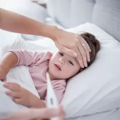 Madre revisa la fiebre de su hija. Si la fiebre persiste, considera el ibuprofeno para bebes.