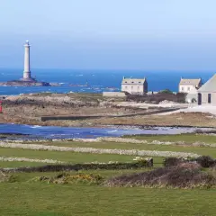 Vue panoramique de la Pointe de la Hague avec son phare emblématique, des maisons de pierre et des champs verdoyants.