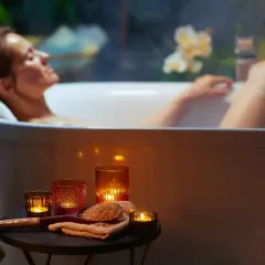 Kobieta relaksuje się w wannie, otoczona świecami i roślinnością. Czas na spokojne zabawy w wannie.
