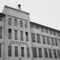 Verlassenes Fabrikgebäude mit der Aufschrift "VOLKSEIGEN", ein Zeugnis der Verstaatlichung in der DDR. Viele Fenster sind zerbrochen.