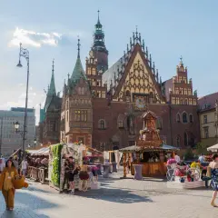 Rynek we Wrocławiu tętni życiem, oferując liczne wrocławskie atrakcje turystyczne. Ludzie spacerują wśród kramów i zabytkowej architektury.