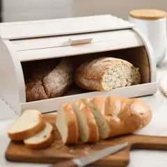 Biały chlebak z dwoma bochenkami w środku i pokrojonym chlebem na desce. Idealne przechowywanie chleba.
