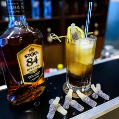 Butelka brandy Stock 84 i drink z cytryną, słomką i żelkami w kształcie butelek.