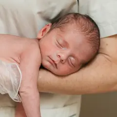 Śpiące niemowlę w ramionach opiekuna. Delikatny dotyk, być może badanie odruchu Babińskiego, wywołuje spokój.