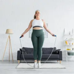 Eine Frau springt mit einem Seil in einem hellen Wohnzimmer. Sie fragt sich, wie oft Sport in der Woche gut ist.
