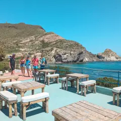 Terraza del cala higuera restaurante con mesas de madera y vistas al mar. Un grupo de amigos disfruta del sol.