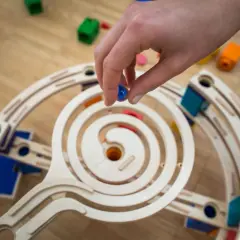 Mano che rilascia una biglia blu su una pista a spirale in legno, parte di giochi con le biglie.
