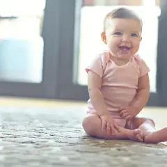 Ein fröhliches Baby sitzt auf einem Teppich und lacht.