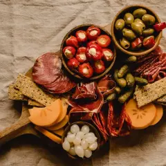 Tabla de que es charcuteria: embutidos, aceitunas, pepinillos, pimientos rellenos, queso y galletas.