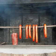 Wędzimy kiełbasę krok po kroku. Wędzone mięso i kiełbaski wiszą w wędzarni, nabierając aromatu dymu.
